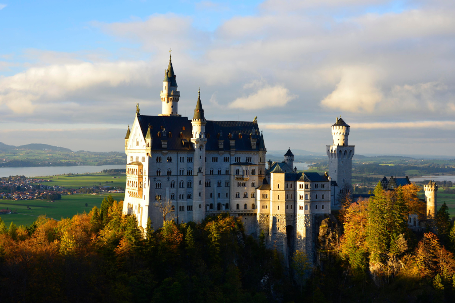 a castle with a clock on the tower of the city with Neuschwanstein Castle in the background