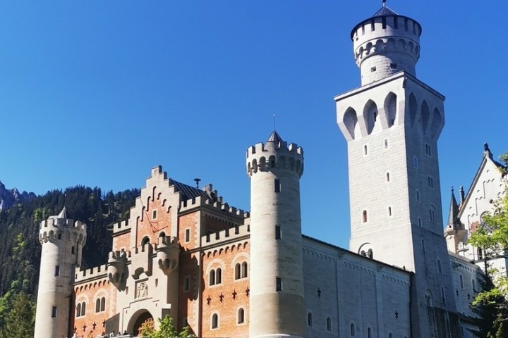 a castle with a clock tower with Neuschwanstein Castle in the background