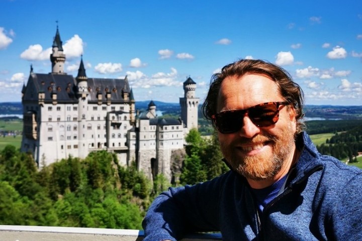 a man wearing sunglasses taking a selfie with Neuschwanstein Castle in the background