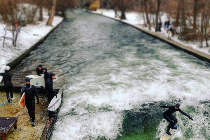 a man riding a wave on a river near a snow covered park