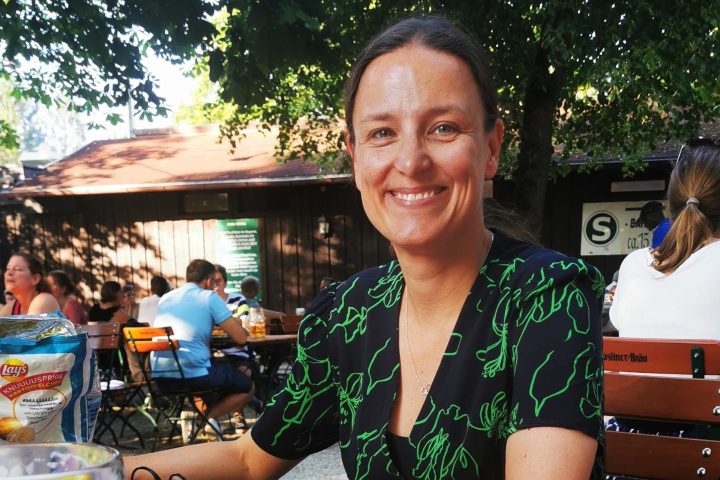 Woman smiling at outdoor table with picnic food and beer on a checkered tablecloth.