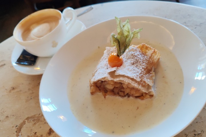 Apple strudel with cream and a coffee on a table.