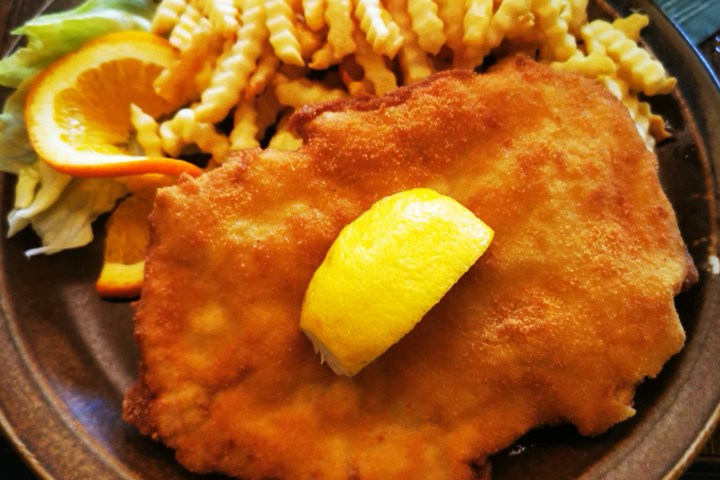 Plate with breaded schnitzel, fries, lemon wedge, lettuce, and orange slices.