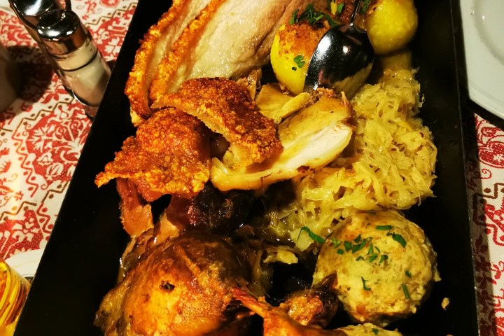 Tray of roasted meat, potatoes, sauerkraut, served on a patterned tablecloth.