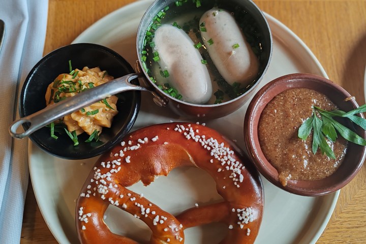 Plate with pretzel, white sausages in broth, mustard, and cheese dip.