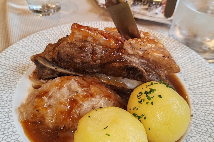 Plate with roasted meat, knife inserted, sauerkraut, and potatoes garnished with herbs.
