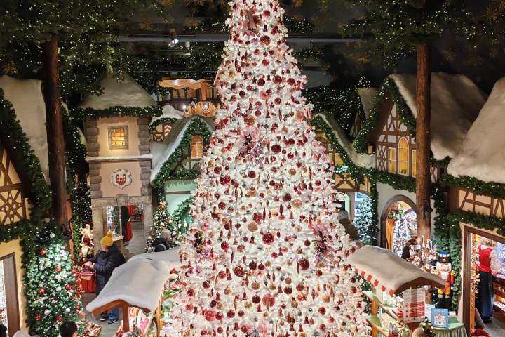 Large white Christmas tree with red ornaments in a festive indoor market setting.
