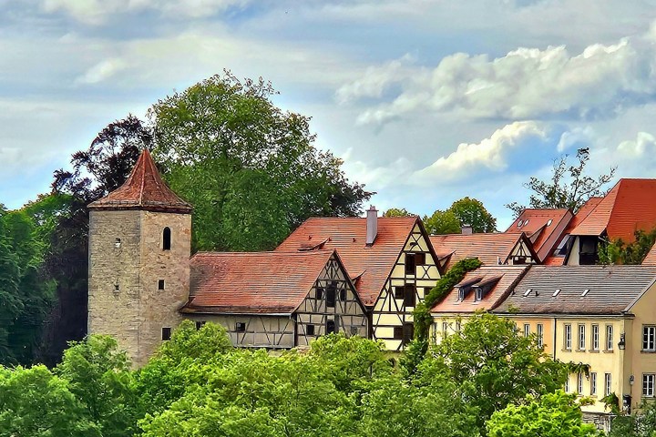 Medieval buildings with red roofs surrounded by trees under a cloudy sky.