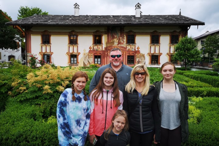 Smiling family in front of a historic building with painted facade in a garden setting.