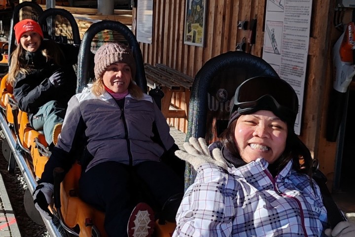 Three women on a mountain coaster smiling and wearing winter clothes.