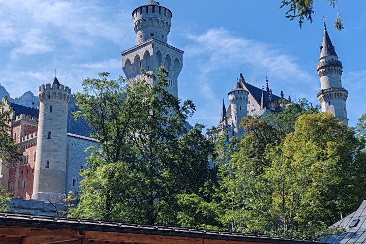 A castle with tall towers surrounded by trees and a wooden shelter with people below.