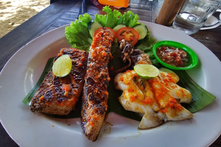 Grilled fish platter with lime, lettuce, tomato, cucumber, and dipping sauce on a white plate.