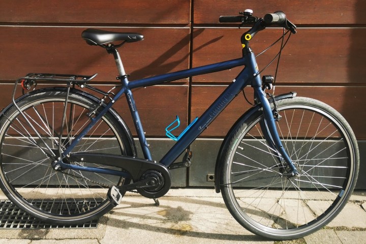 A blue bicycle parked against a wooden wall in sunlight.