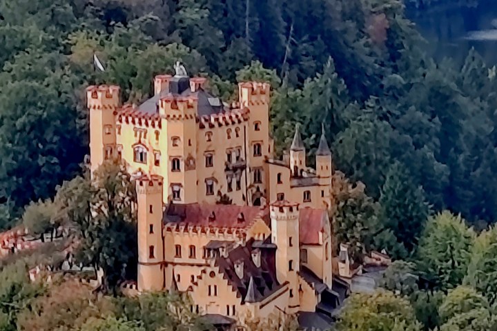 Aerial view of a yellow castle surrounded by dense green trees.