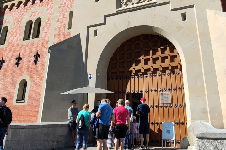 People standing outside a large wooden arched door on a brick building.