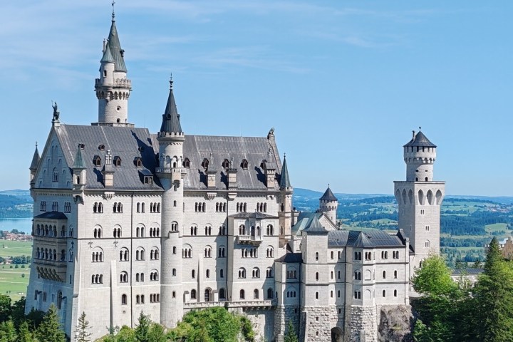 Neuschwanstein Castle in Bavaria, Germany, with blue sky and lush greenery.