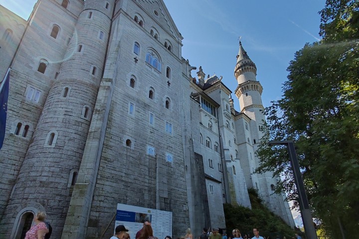 People gathered near a large stone castle with towers under a clear blue sky.