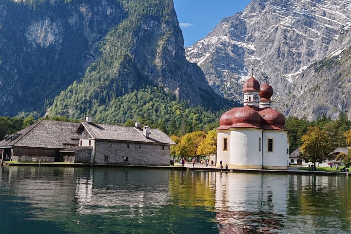 Lake with chapel and mountains in the background under a blue sky.