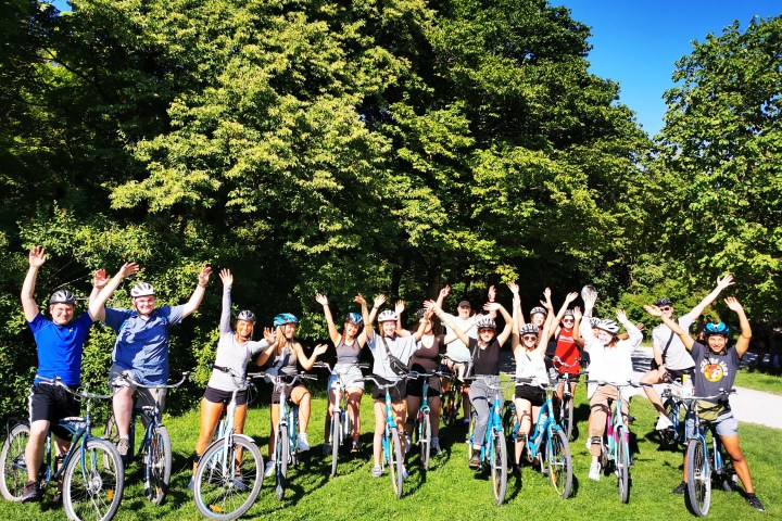 Group of cyclists with raised arms on a sunny day in a park.
