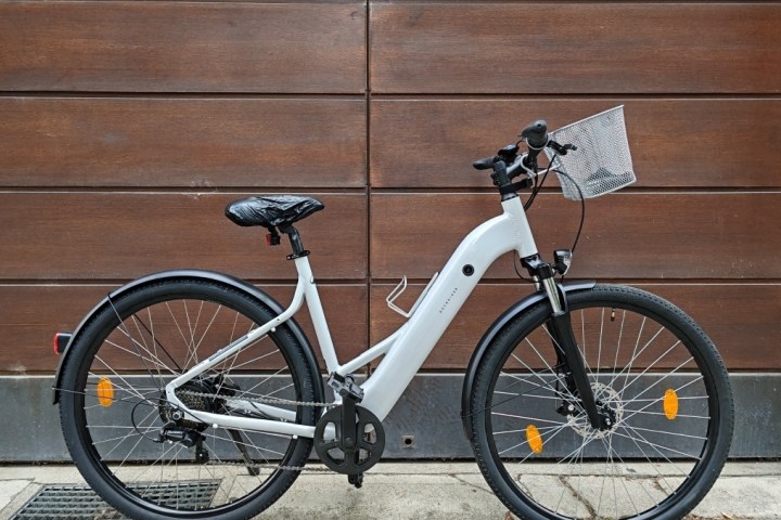White bicycle with basket parked against a wooden wall.