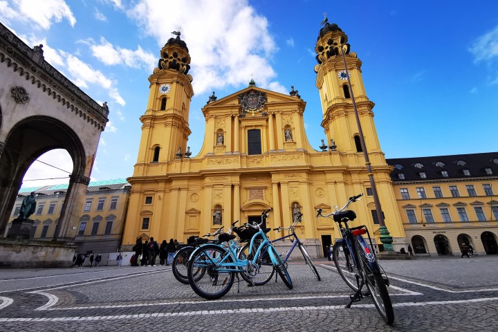 Yellow baroque church facade with two towers, view from square with parked bicycles.