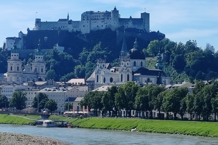 Historic fortress on a hill overlooking a European city by a river on a sunny day.