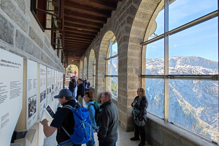 Visitors reading historical displays inside a stone building with arched windows offering mountain views.