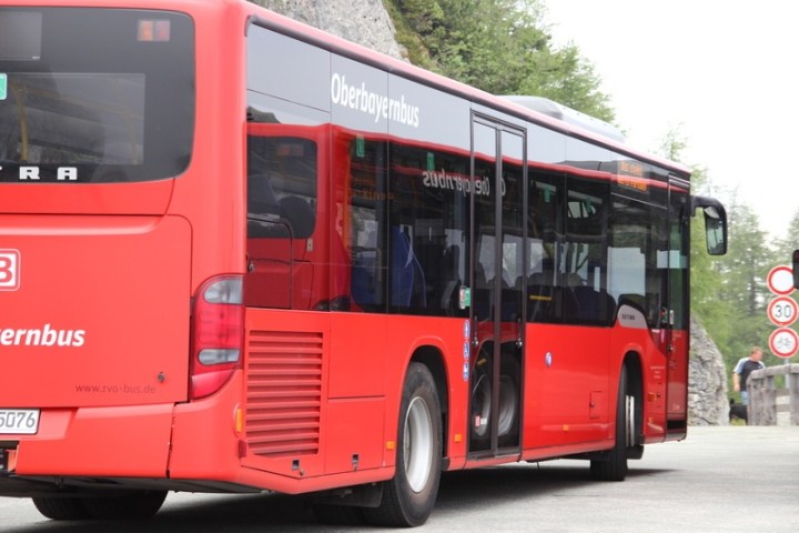 Red Oberbayernbus on a road with traffic signs and trees in the background.