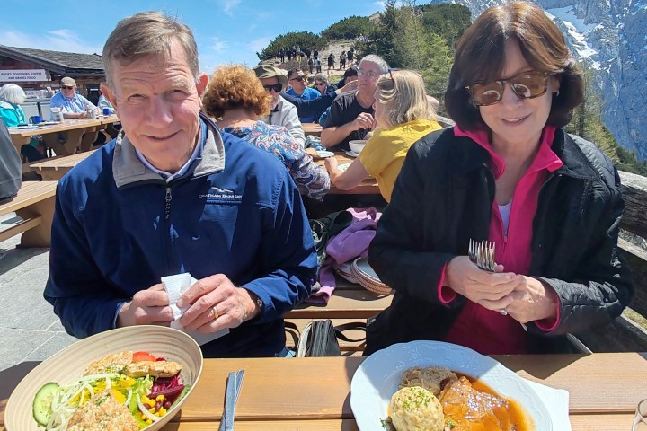 A couple sitting outdoors at a table enjoying a meal with mountains in the background.