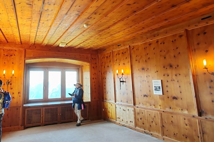 Two people in a wooden-paneled room with a window, reading and taking photos.