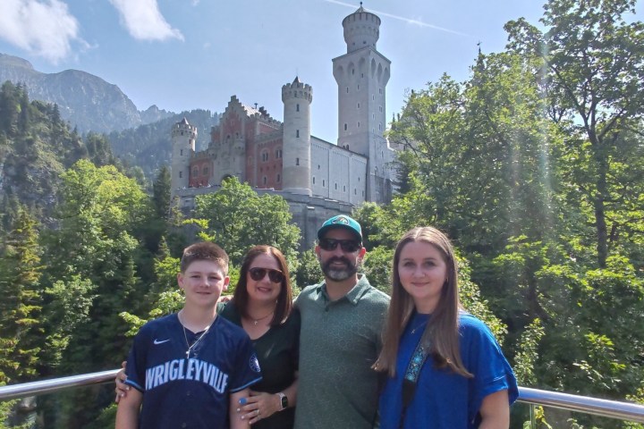 Family posing in front of a castle set in a lush, mountainous landscape.