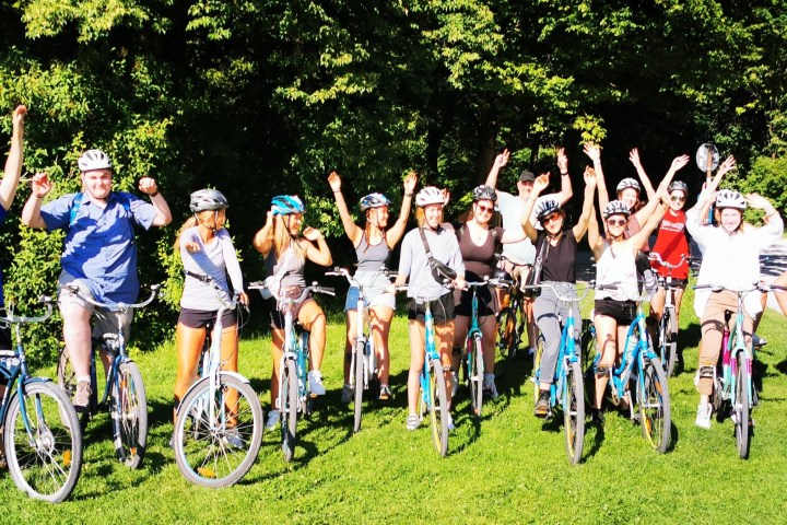 Group of cyclists with raised arms posing in a sunny park.