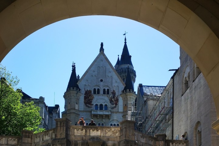 Castle viewed through an arch with blue sky and trees.