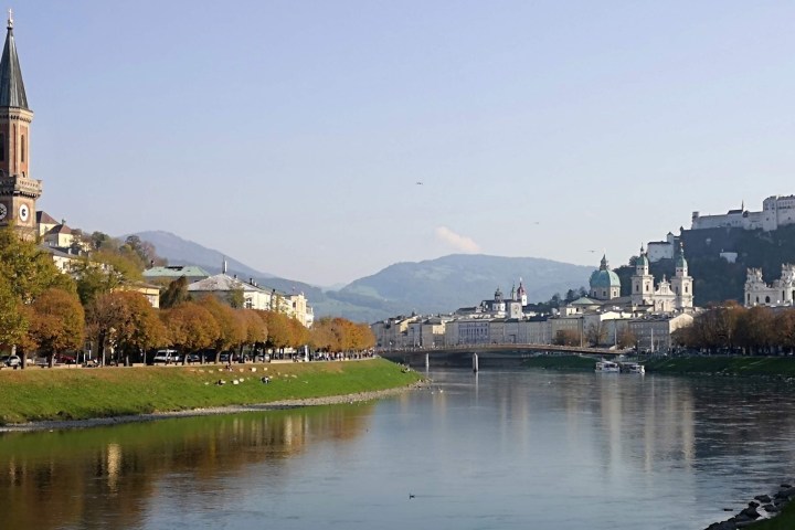 View of Salzburg river with church, fort on hill, and distant mountains on a clear day.