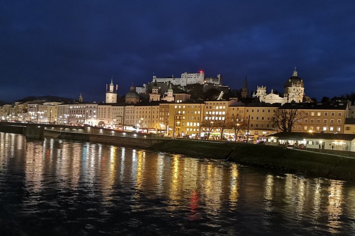 Night view of city skyline with illuminated buildings and a river reflecting lights.