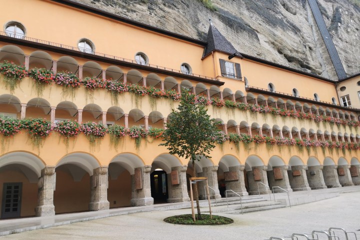 Historic building with arched balconies and hanging flowers, set against a rocky cliff.