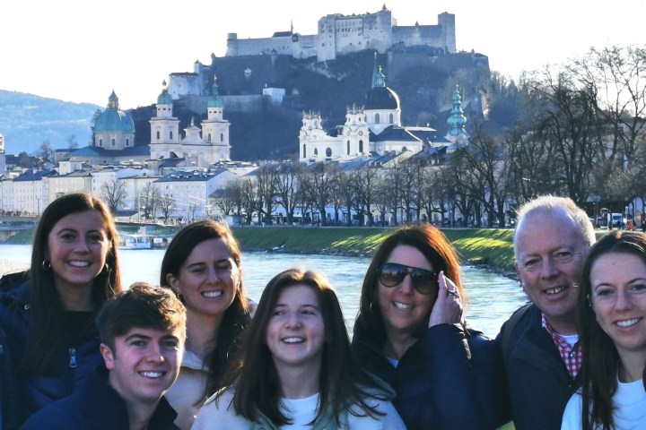 Group of people smiling by a river with a castle and cityscape in the background.