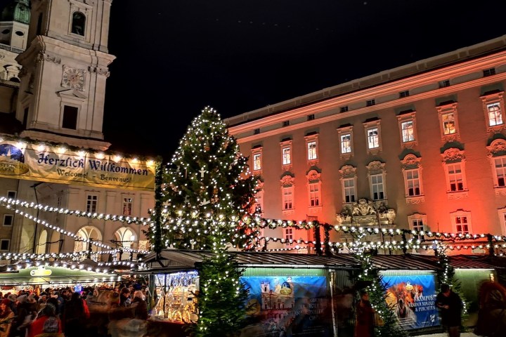 Festive Christmas market with lights, tall tree, and illuminated buildings at night.