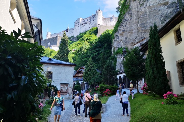 Tourists walking on a cobblestone path with a castle on a hill in the background.