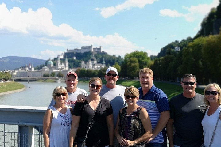 Group of seven people posing on a bridge with a city and castle in the background.