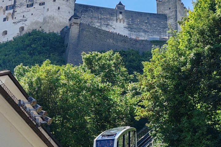Modern funicular ascending a hillside with a large historic castle on top.