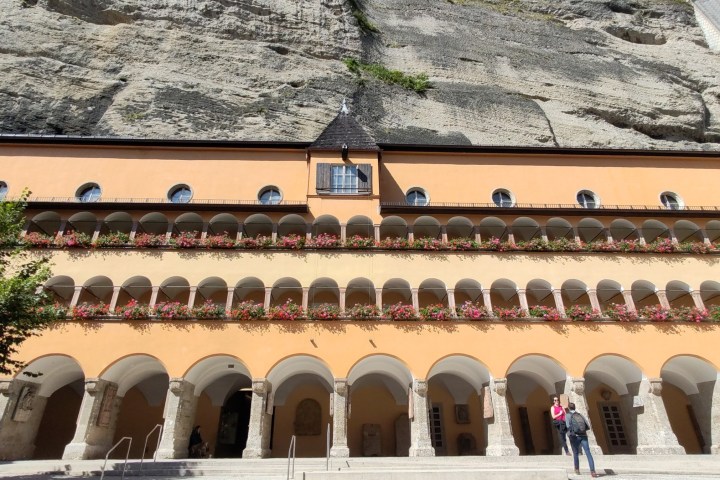 Historic building with arched balconies and flowers, set against a rock cliff.