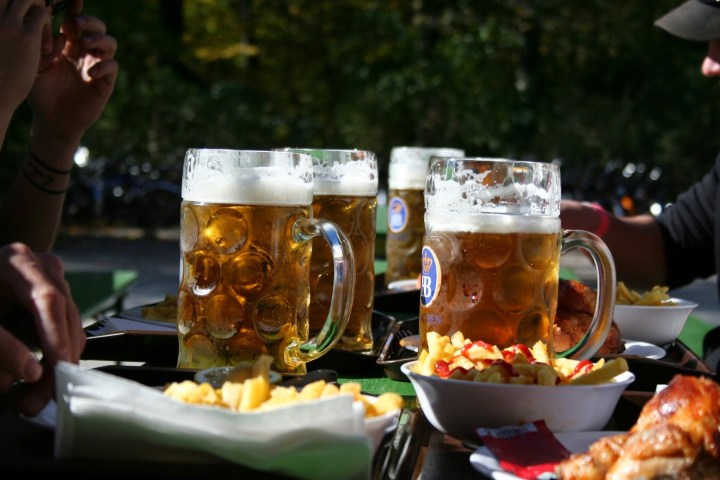 Large steins of beer with fries and chicken on an outdoor table.