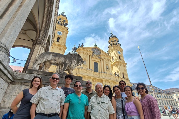Group of people posing in front of a historical building with towers and a lion statue.