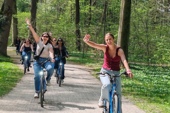 Group of people cycling on a forest path, waving and smiling.