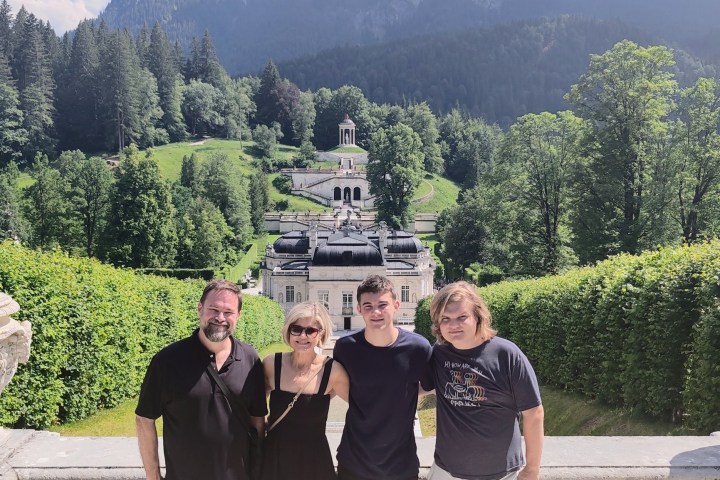 Four people posing in front of a scenic hillside with a historic building.