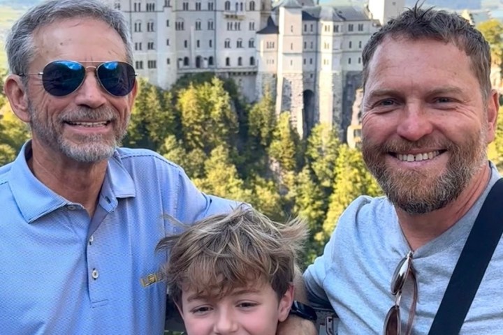 Three people smiling in front of a castle on a sunny day.